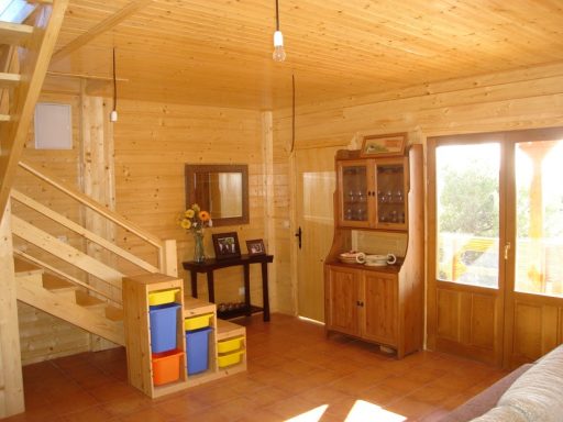 Interior de una cabaña de madera con escaleras, muebles y grandes ventanales.