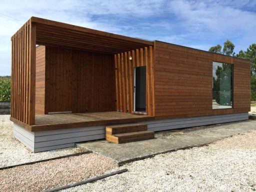 Casa prefabricada moderna de madera con patio y grandes ventanas, ubicada en un entorno natural.