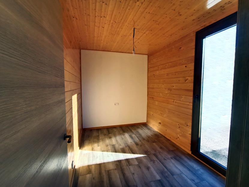 Habitación vacía con paredes de madera y una ventana que deja entrar luz.