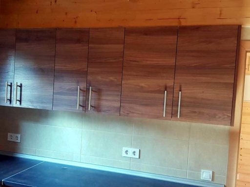 Muebles de cocina con gabinetes de madera clara y tiradores metálicos en una pared.