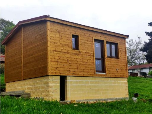 Casa prefabricada con base de piedra, ubicada en un entorno verde y nublado.