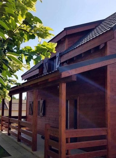 Casa prefabricada de madera con terraza, tejado a dos aguas y entorno verde.