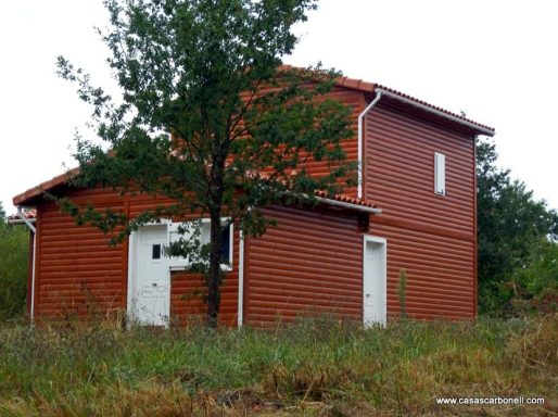 Casa prefabricada de dos plantas de color rojo con árbol y hierba alrededor.