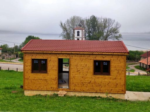 Casa prefabricada con techo de tejas en un entorno verde junto a un lago.