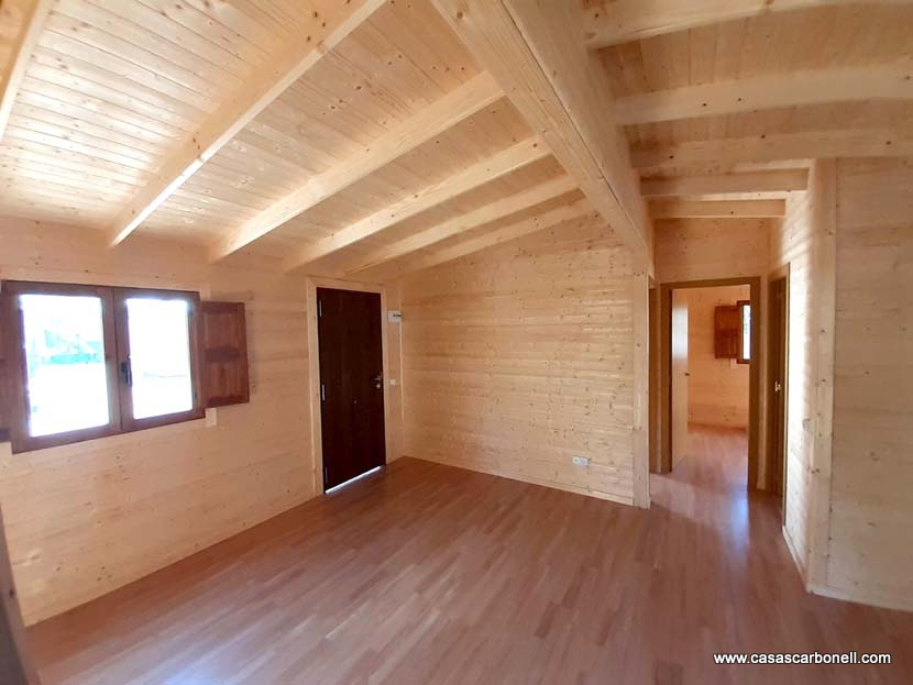Interior de una casa de madera con techos altos y ventanas claras. Suelo de madera.