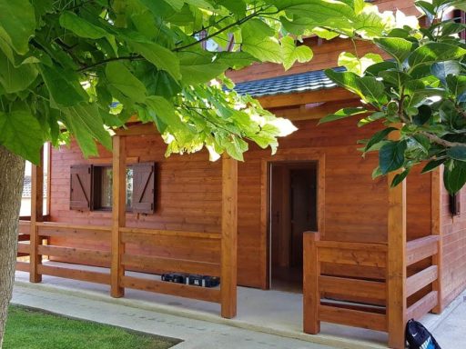 Casa prefabricada de madera con porche y vegetación verde alrededor.