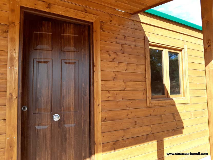 Puerta de madera oscura junto a una ventana en una pared de madera clara.