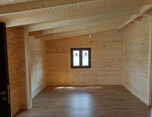 Interior de una habitación con paredes de madera y una ventana pequeña. Suelo de madera.