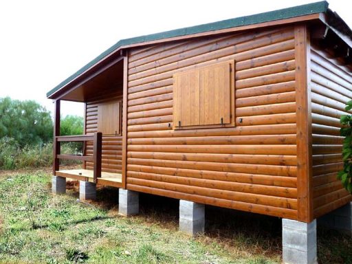 Casa prefabricada de madera con acabado en tonos marrones, situada sobre soportes en un entorno natural.