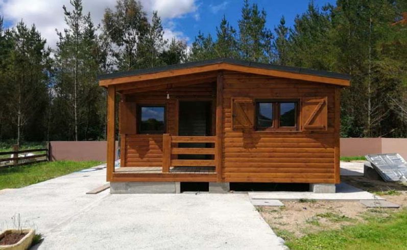 Casa prefabricada de madera con ventanas y puerta frontal, rodeada de vegetación.