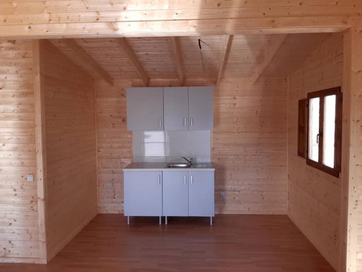 Cocina moderna en una cabaña de madera con armarios y ventanas abiertas.