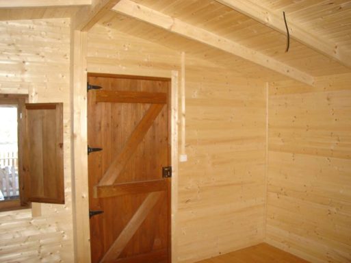 Interior de una cabaña de madera con paredes claras y puerta de madera.