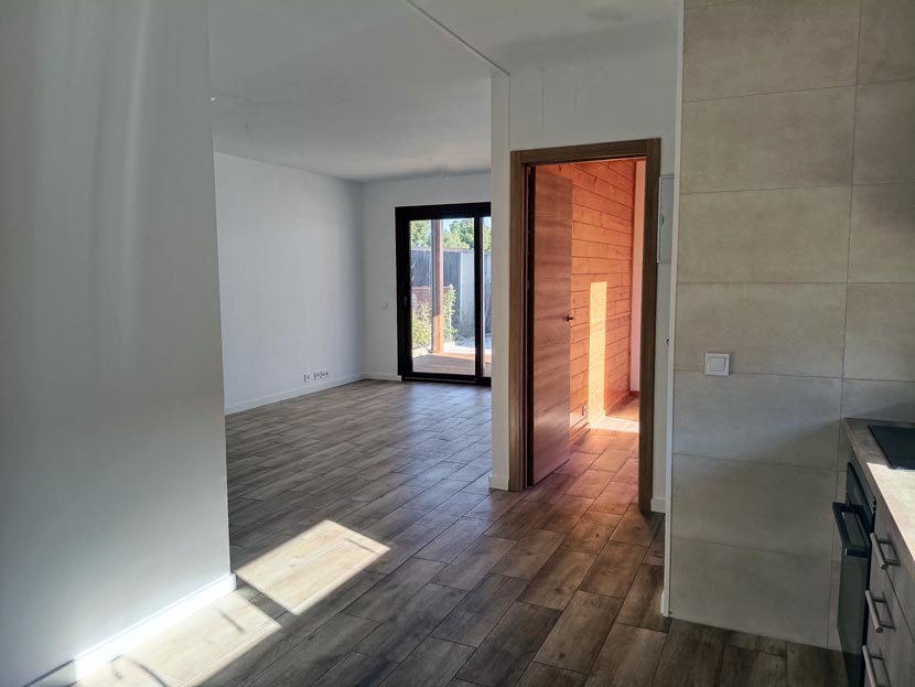 Interior de una habitación con suelo de madera, puertas y luz natural entrando.