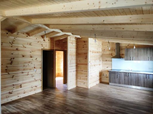 Interior de una casa de madera con paredes y techo de tablones, cocina y suelos de madera.