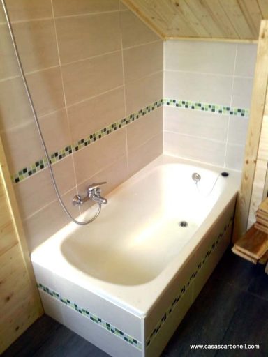 Bañera blanca con grifo, ubicada en un baño con paredes de madera y azulejos verdes.