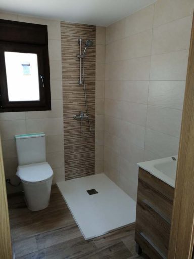 Baño moderno con ducha, inodoro y mueble de lavabo en tonos claros.