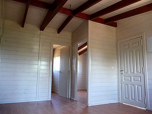 Interior de una casa con paredes blancas, techos de madera y una puerta en la esquina.