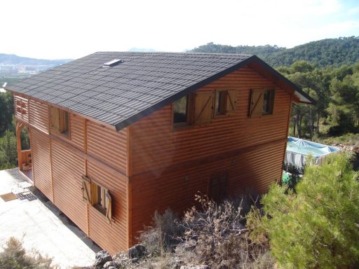 Casa prefabricada de estilo moderno con paredes de madera, rodeada de montañas y vegetación.