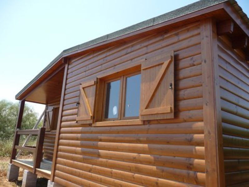 Casa prefabricada de madera con ventanas con persianas y un porche frontal.