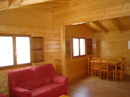 Interior de una cabaña de madera con sillón rojo y mesa de comedor.