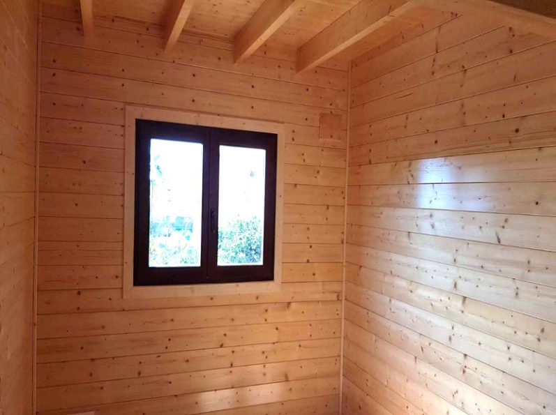 Interior de una habitación de madera con una ventana y paredes de paneles de madera.
