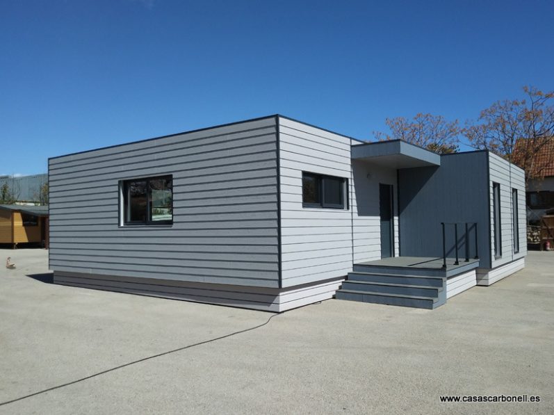 Casa prefabricada moderna de un solo piso con revestimiento gris y escaleras de acceso.