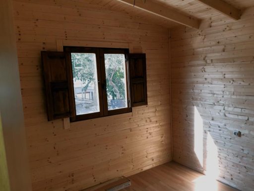 Interior de una habitación con paredes de madera y ventana abierta al exterior.