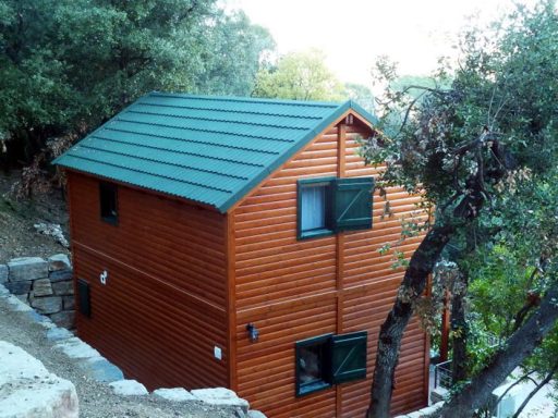 casa prefabricada de madera de color naranja con techo verde, situada en un entorno natural.