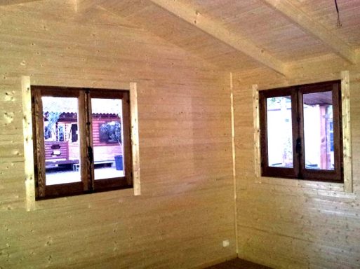 Interior de una habitación con paredes de madera y dos ventanas con marcos oscuros.