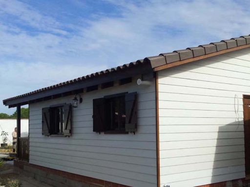 Casa prefabricada de una planta con ventanas oscuras y tejado a dos aguas bajo un cielo azul.