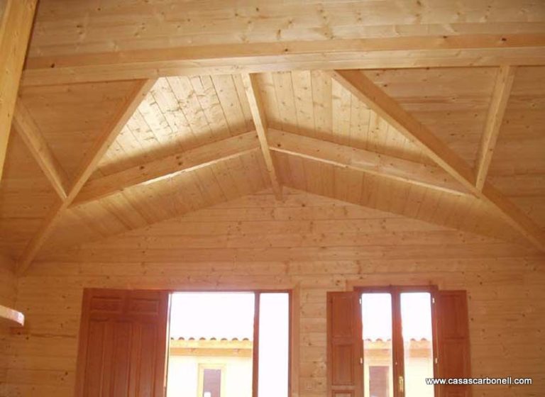 Techo de madera con vigas en ángulo en una habitación con ventanas.