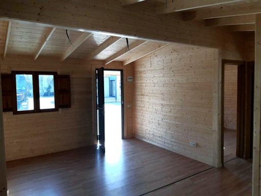 Interior de una cabaña de madera con ventanas y un suelo de madera clara.