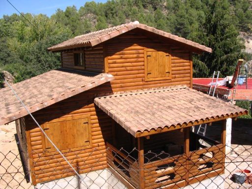 Casa prefabricada de madera de dos plantas con techos a dos aguas y porche, rodeada de vegetación.