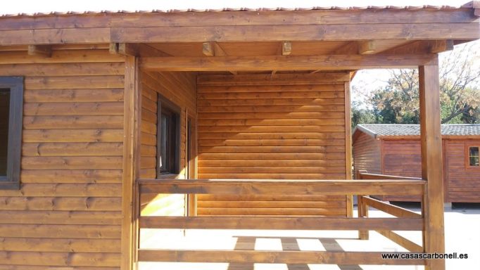 Casa prefabricada de madera con porch, techado de tejas y detalles en madera natural.