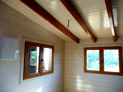 Interior de una habitación con paredes claras y ventanas de madera iluminadas.