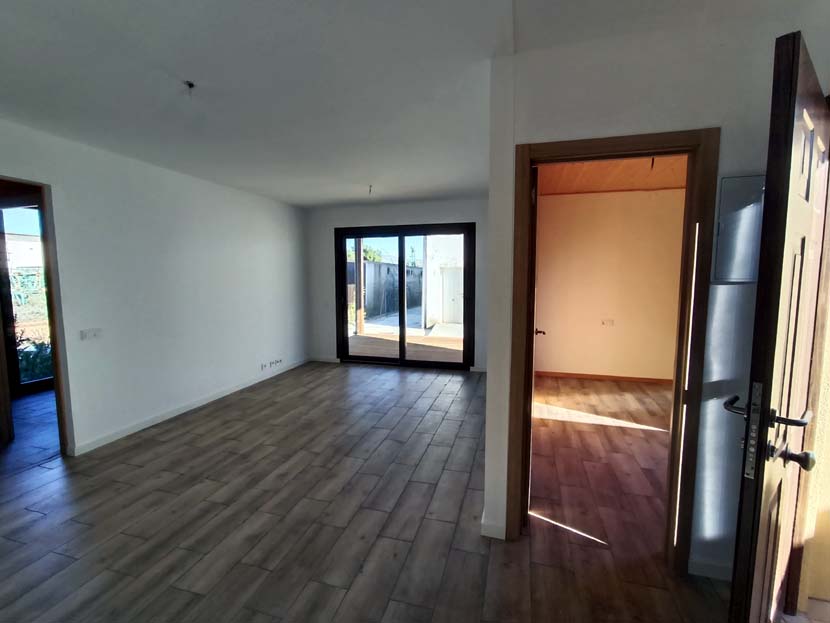 Interior de una habitación vacía con suelo de madera, puertas abiertas y luz natural.