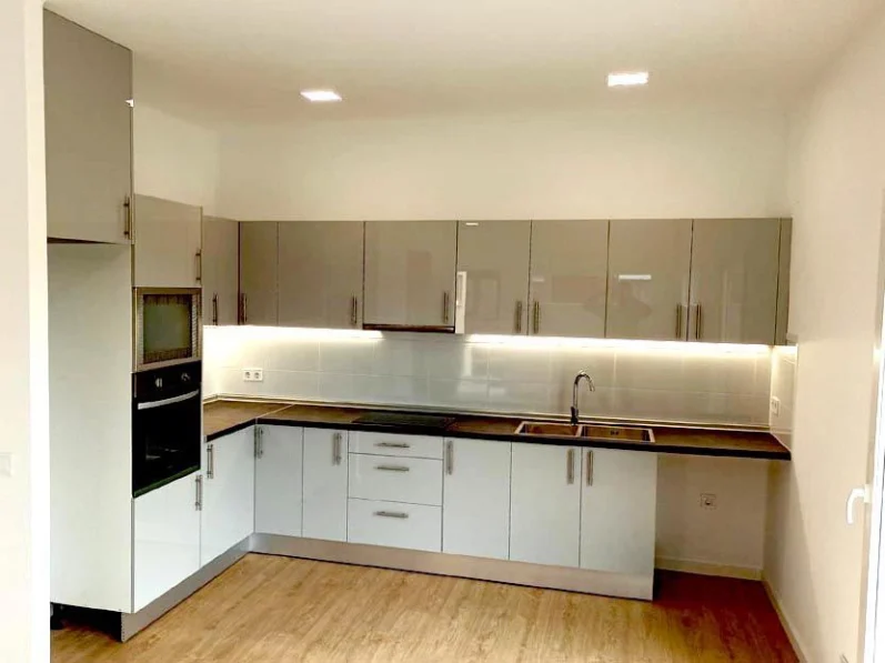 Cocina moderna con muebles blancos y grises, encimera de madera y azulejos claros.