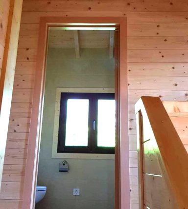 Puerta con espejo en una pared de madera, ventana con vistas al exterior y escalera cercana.