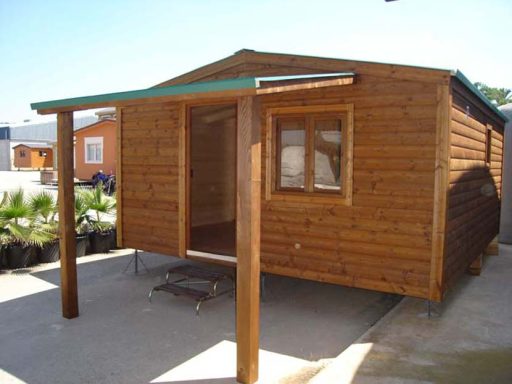 Casa de madera con porche y techo a dos aguas, ubicada en un entorno rural.