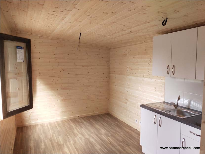 Interior de una habitación con paredes de madera clara y una pequeña cocina equipada.