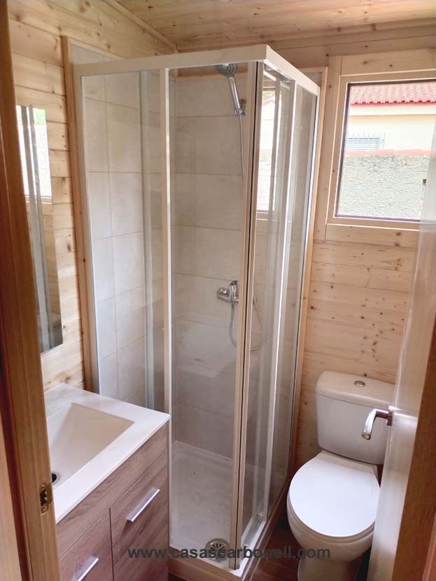 Baño pequeño con ducha, lavabo y sanitario en un ambiente de madera.