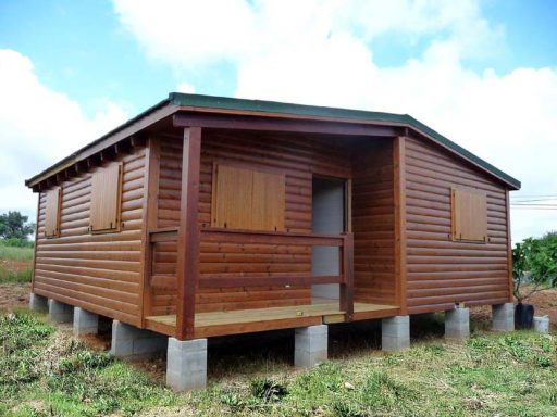 Casa prefabricada de madera con puertas y ventanas cerradas, situada sobre pilotes en un terreno rural.