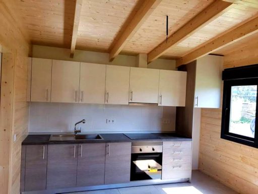 Cocina con muebles de madera clara y encimera oscura en una casa de madera.