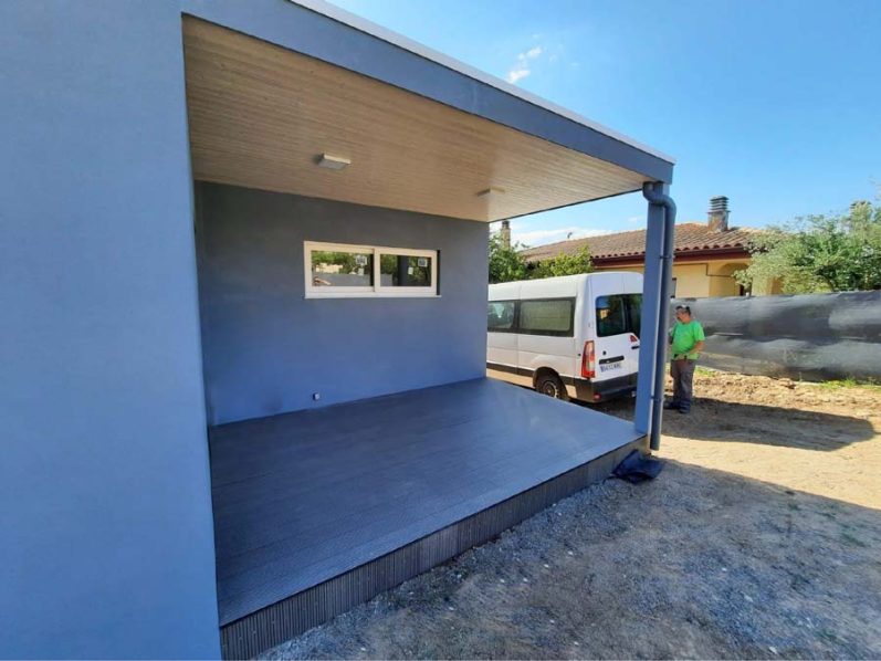 Casa moderna de un espacio exterior con una pared azul y una furgoneta blanca al fondo.