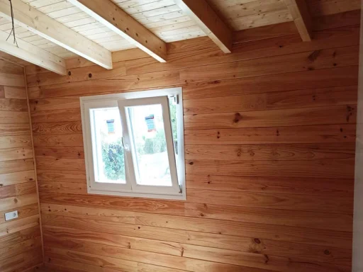 Interior de una habitación con paredes de madera y una ventana blanca.