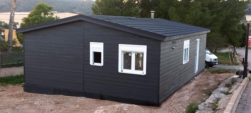 Casa prefabricada moderna de color negro con ventanas blancas, situada en un entorno natural.