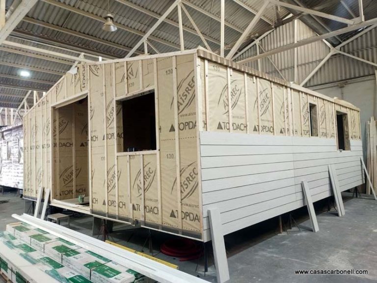 Casa prefabricada en proceso de revestimiento con lamas de fibrocemento Estructura de una casa prefabricada en construcción, con paneles de madera y ventanas sin colocar.