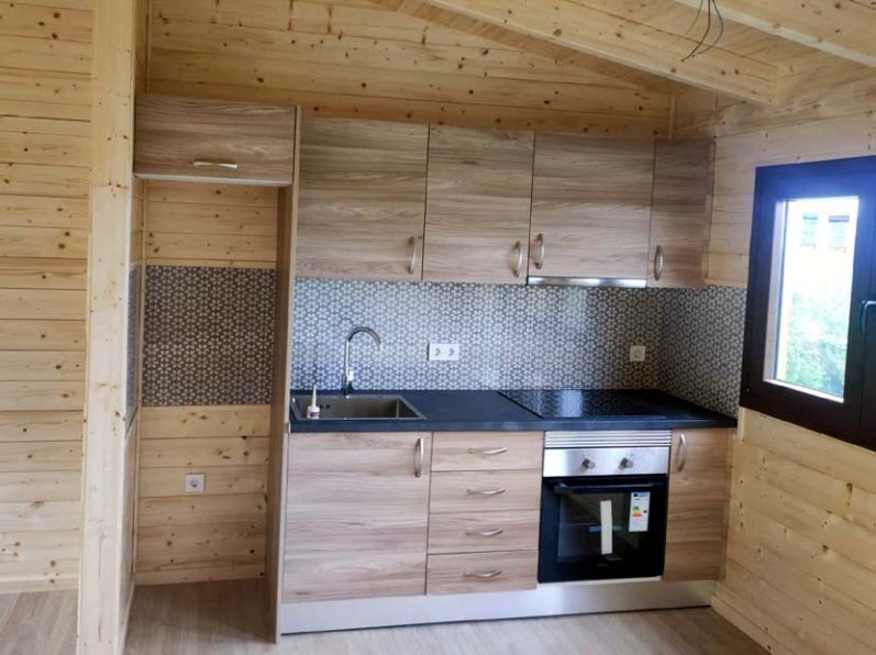 Cocina moderna de madera con muebles claros, encimera oscura y electrodomésticos integrados.