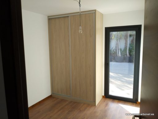 Habitación con armario de madera y puerta de cristal que da al exterior.