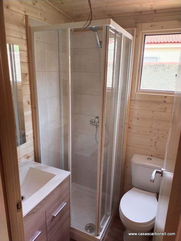 Baño pequeño con ducha, lavabo y inodoro en un entorno de madera.
